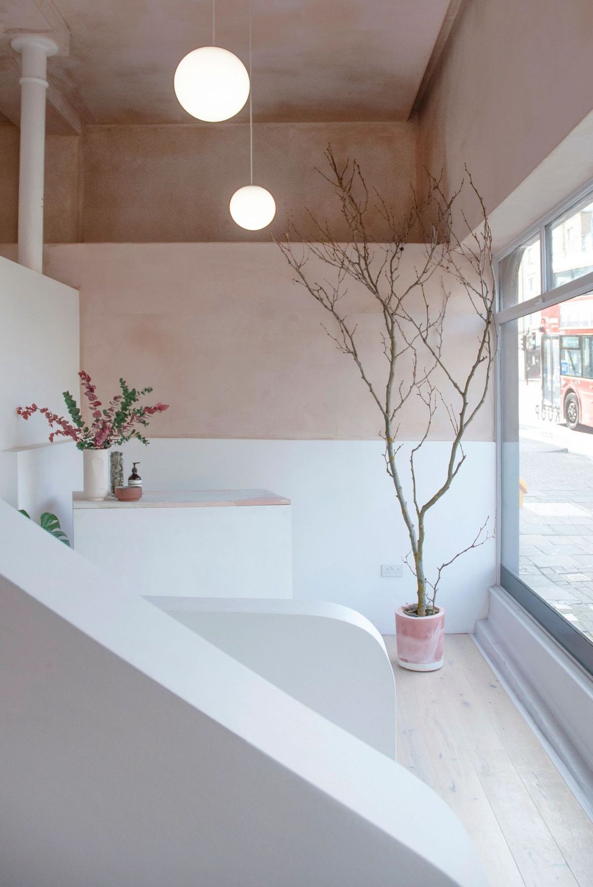 The KOOP Studio reception, with a large street window, a potted tree and a curved white staircase
